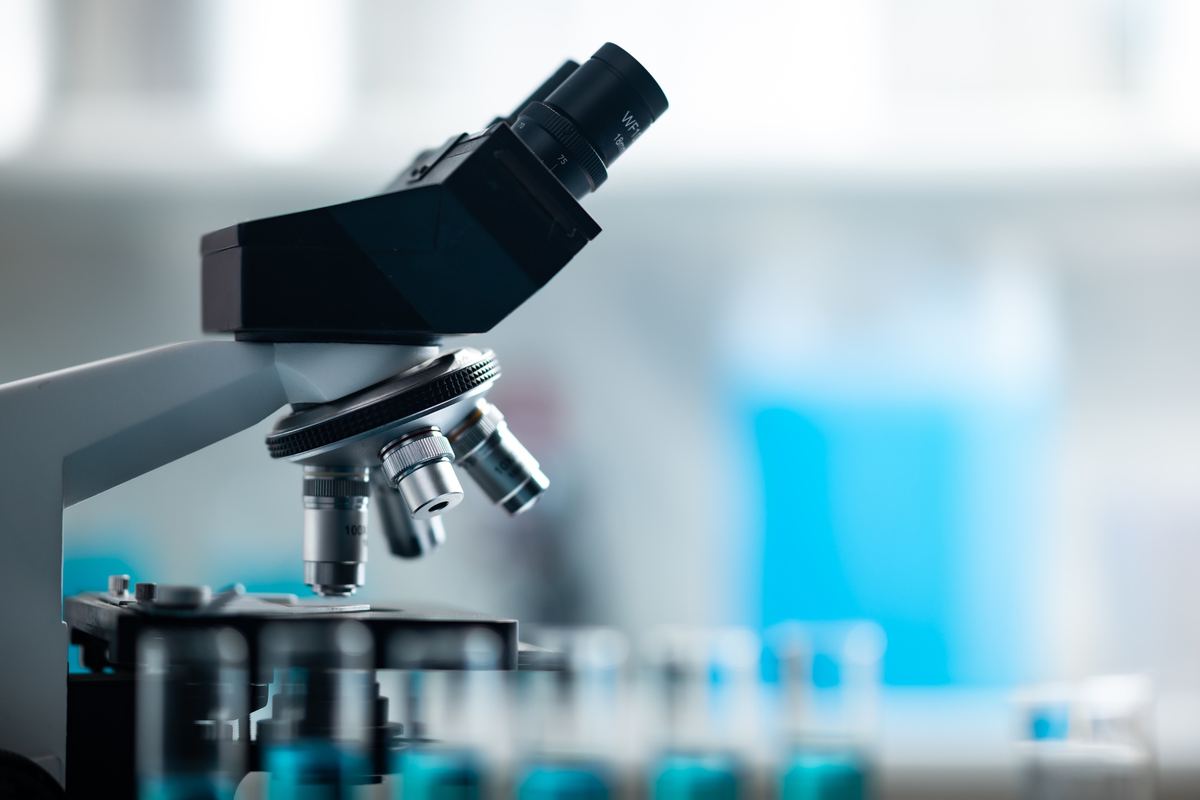 A laboratory microscope with test tubes in the background